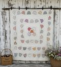 A quilted fabric panel featuring butterfly appliques in various colors and patterns, hung on a rustic white wooden wall. A wicker basket labeled 'Janj Threads' sits on the left, and a basket of flowers sits on the right.