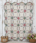 A handmade quilt with a scalloped edge, featuring a repeating pattern of interlocking circles and diamonds in multicolored floral fabrics on an off-white background. The quilt is displayed against a rustic white-painted wooden wall, flanked by two wicker baskets containing dried flowers and small wooden beads.